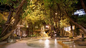An indoor garden with a central water feature, stone benches, and a statue.