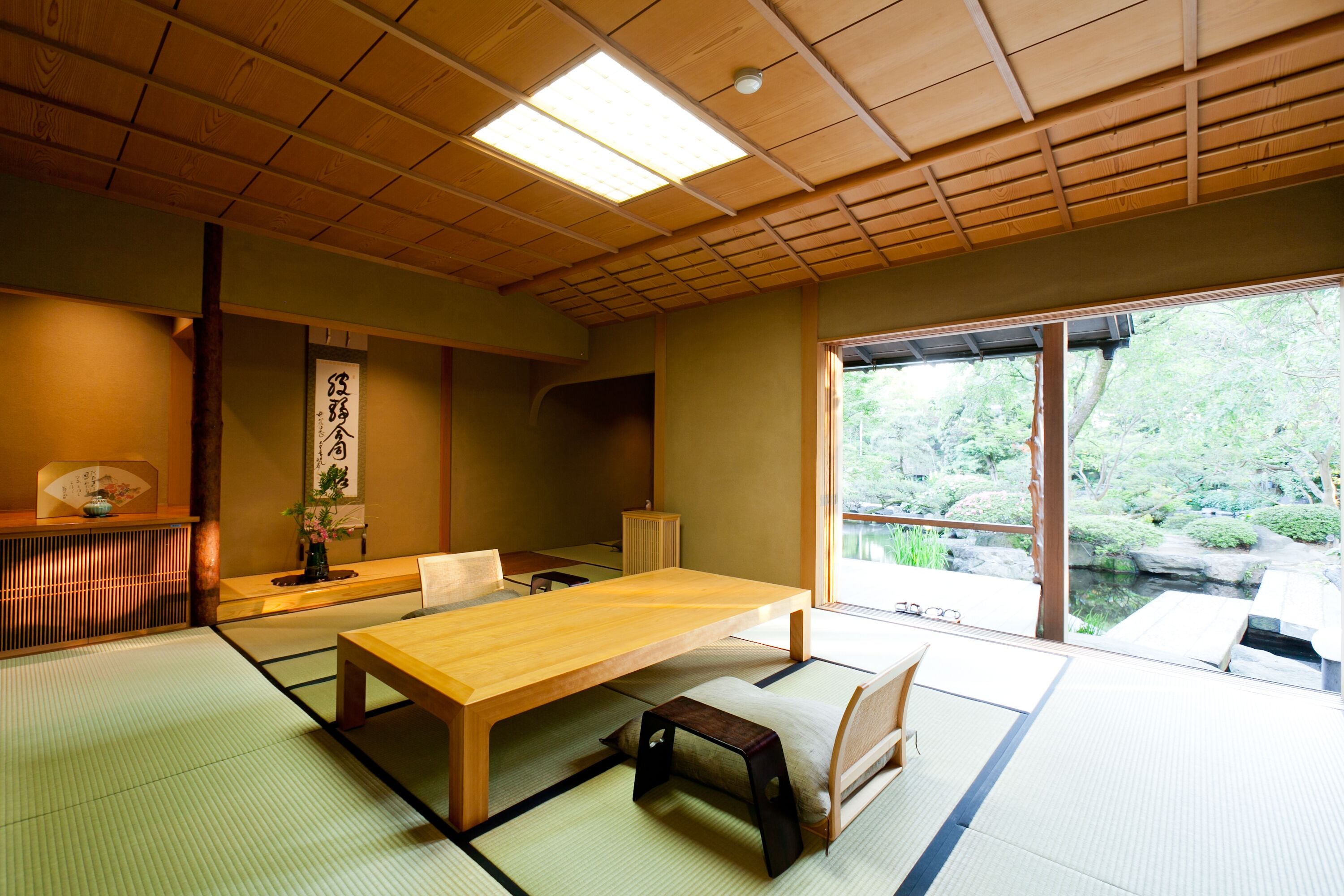 A traditional Japanese room with tatami flooring, a low wooden table, and a view of a garden through a sliding door.