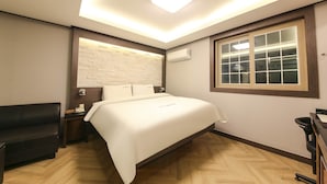 Una habitación de hotel con cama, escritorio, silla, ventana y aire acondicionado.