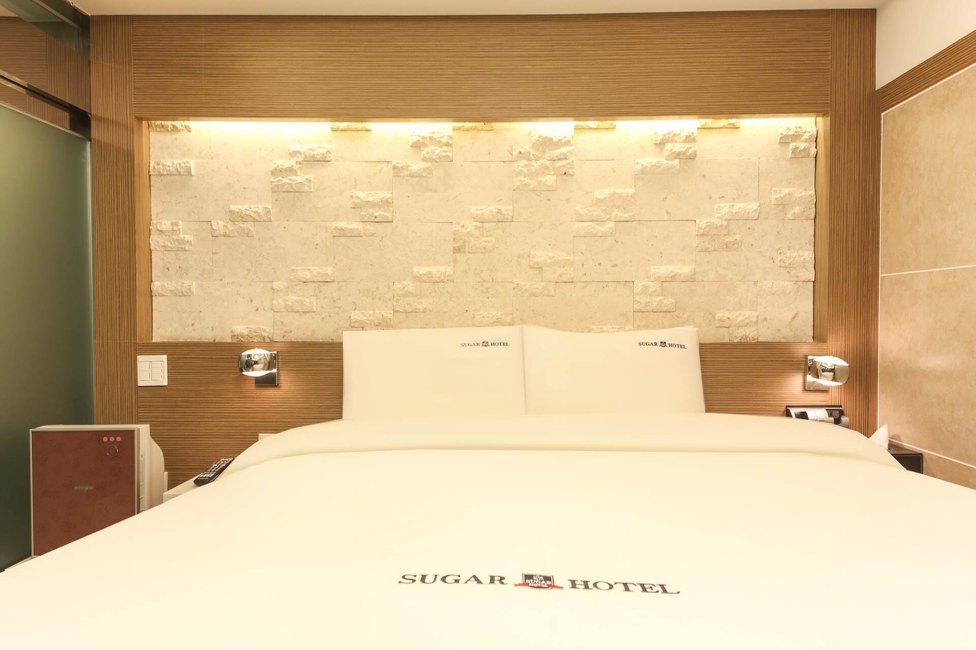 Una habitación de hotel con una cama grande, un cabecero de madera con diseño de piedra texturizada y dos lámparas de noche.