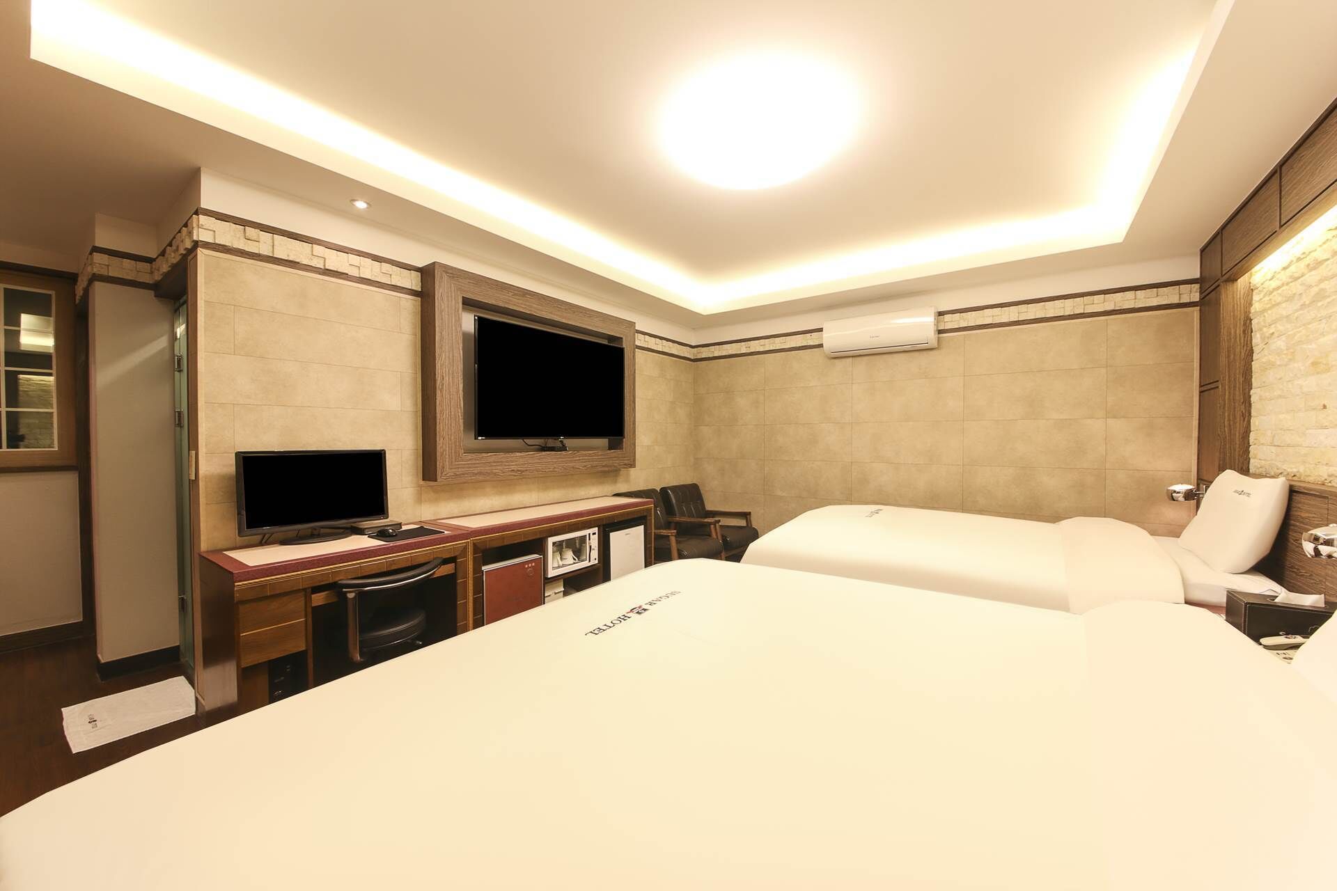 Habitación de hotel con una cama grande, un escritorio con computadora, un televisor de pantalla plana en la pared y una pequeña zona de estar con sillas.