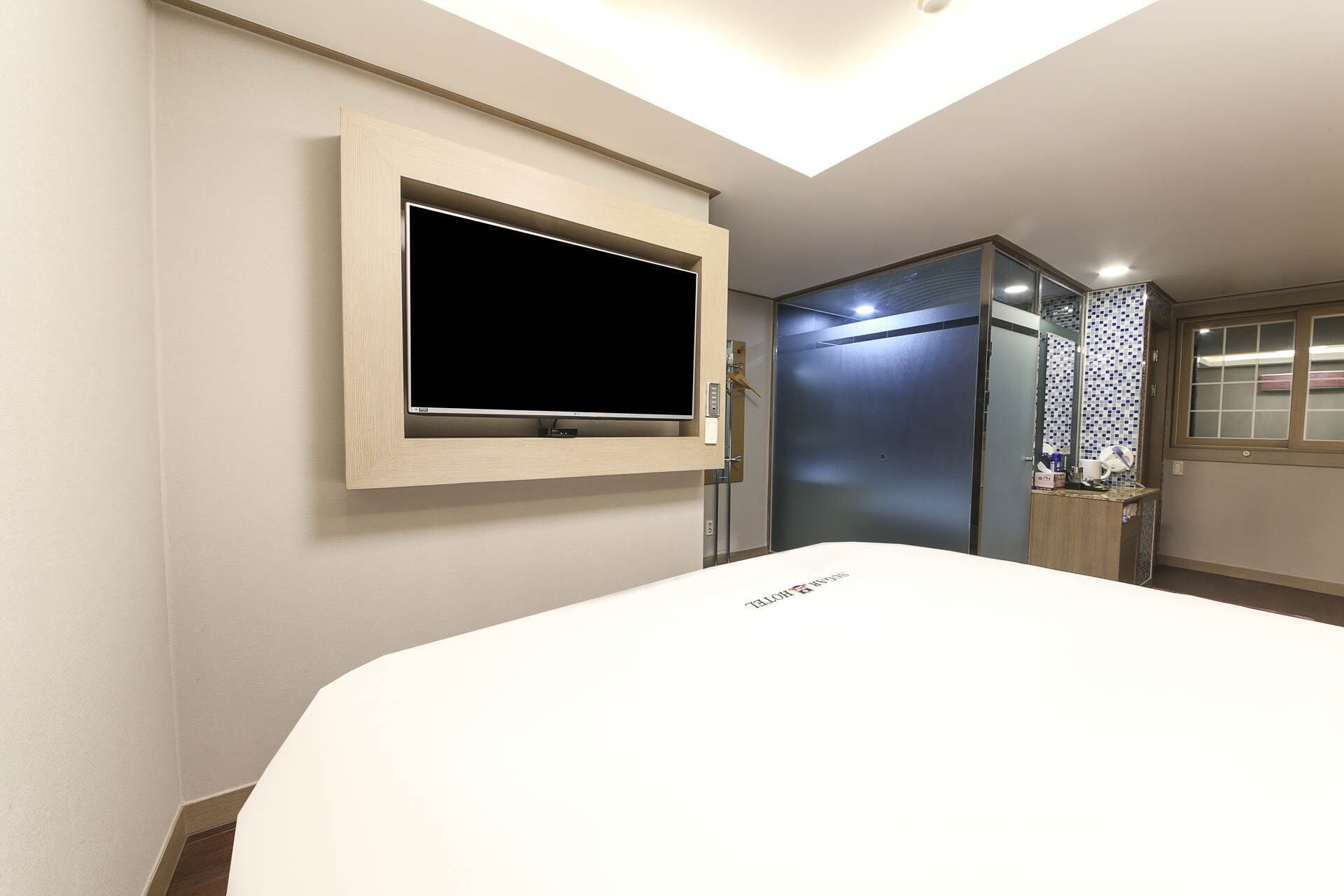 A hotel room with a large bed, a mounted TV, a walk-in closet, and a bathroom with a mirror and tiled backsplash.