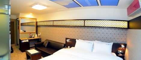 A hotel room with a bed, a desk, a chair, a nightstand, and a mirror.
