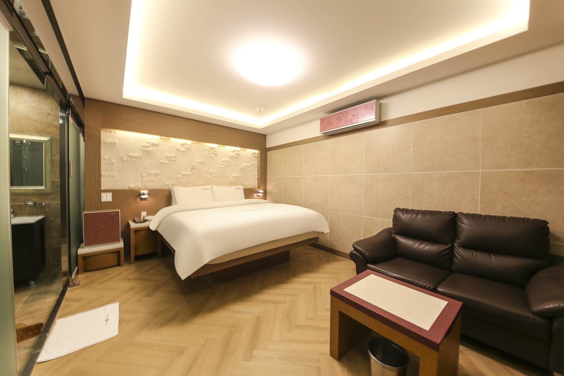 Une chambre d’hôtel avec un lit, un canapé en cuir, une petite table et un miroir.