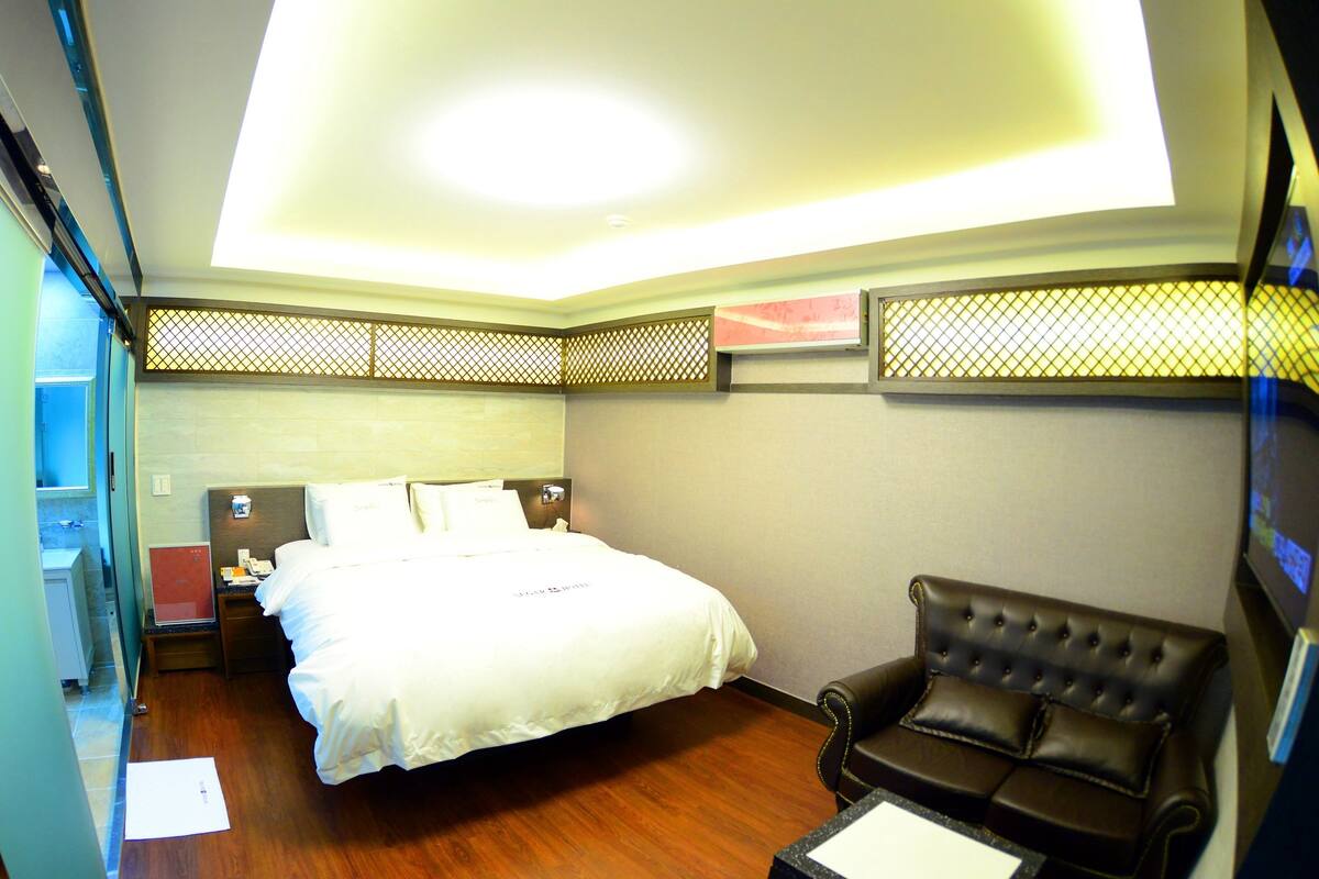 A hotel room with a bed, a leather sofa, a nightstand, and a desk with a computer.