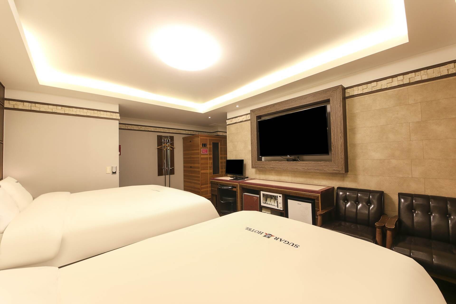 A hotel room with a large bed, a desk with a flat-screen TV, a seating area with a leather couch, and a minibar.