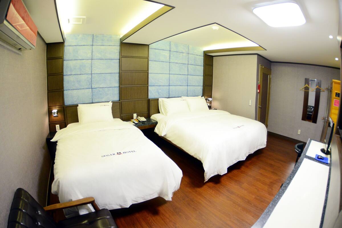 A hotel room with two beds, a desk, and a mirror.
