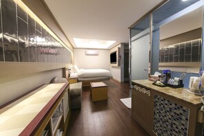 A hotel room with a bed, a small table, a mirror, and a bathroom with a sink and toiletries.