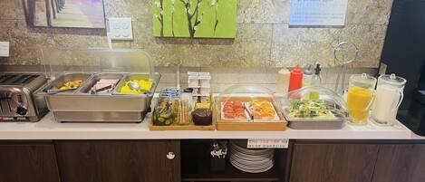 A buffet counter with various food options, condiments, and utensils.