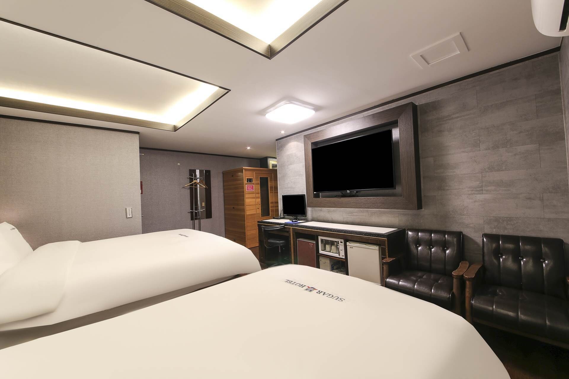 Ein Hotelzimmer mit zwei Betten, einem Schreibtisch mit Computer, einem Fernseher und einer Sitzecke mit Ledersesseln.