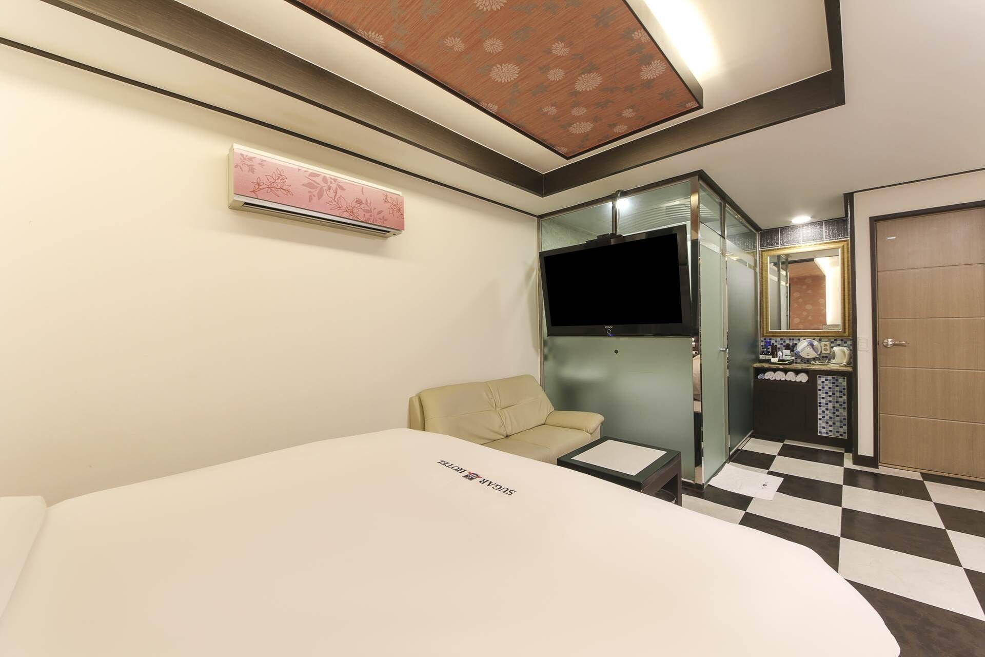 A hotel room with a bed, a sofa, a TV, a mirror, and a bathroom with a checkered floor.