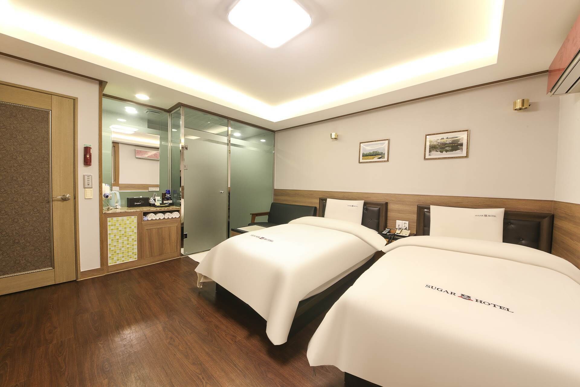 Ein Hotelzimmer mit zwei Betten, einem kleinen Schreibtisch, einem Spiegel und einer Tür zum Badezimmer.