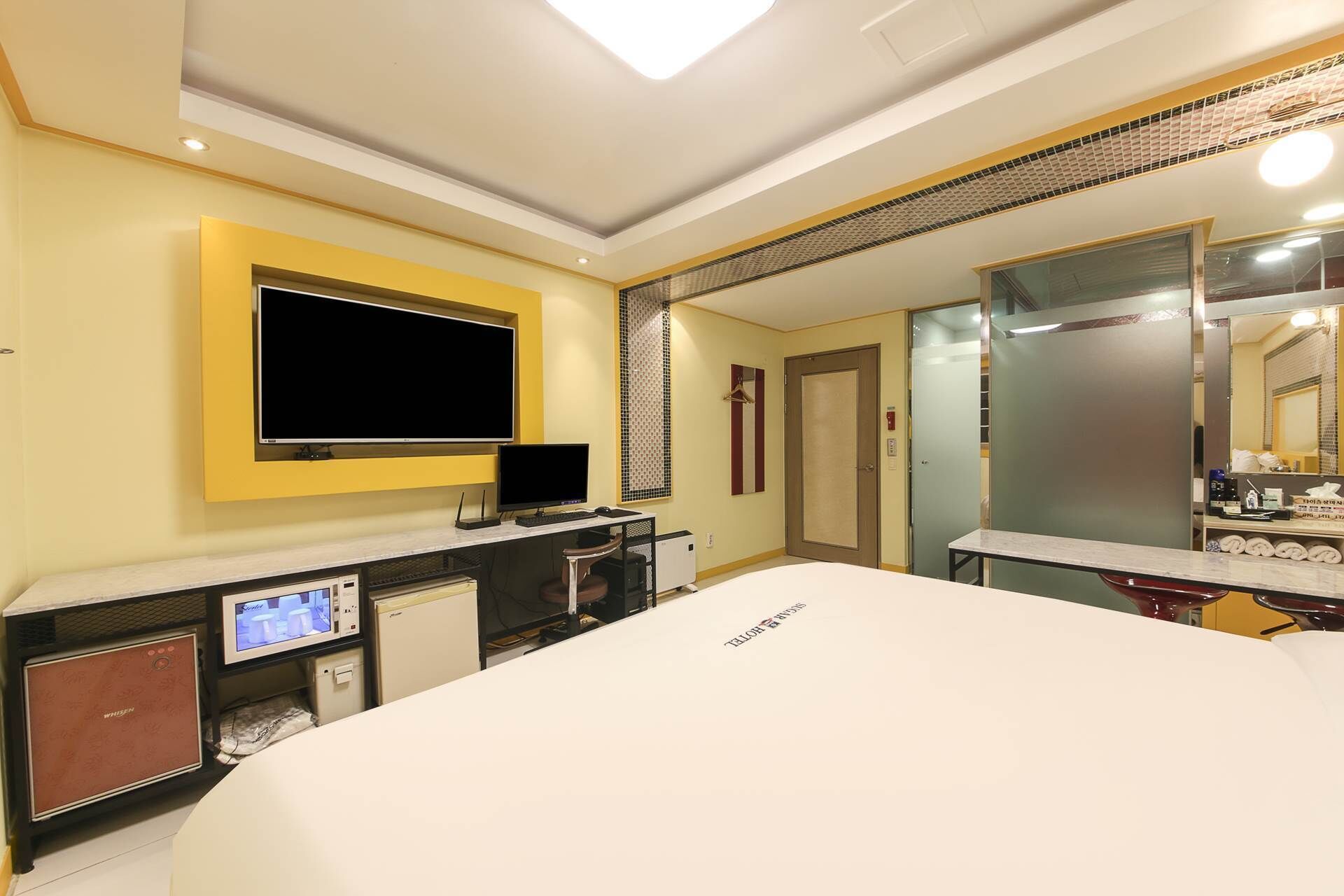 Una habitación de hotel con una cama grande, un escritorio con computadora, televisor y minibar.