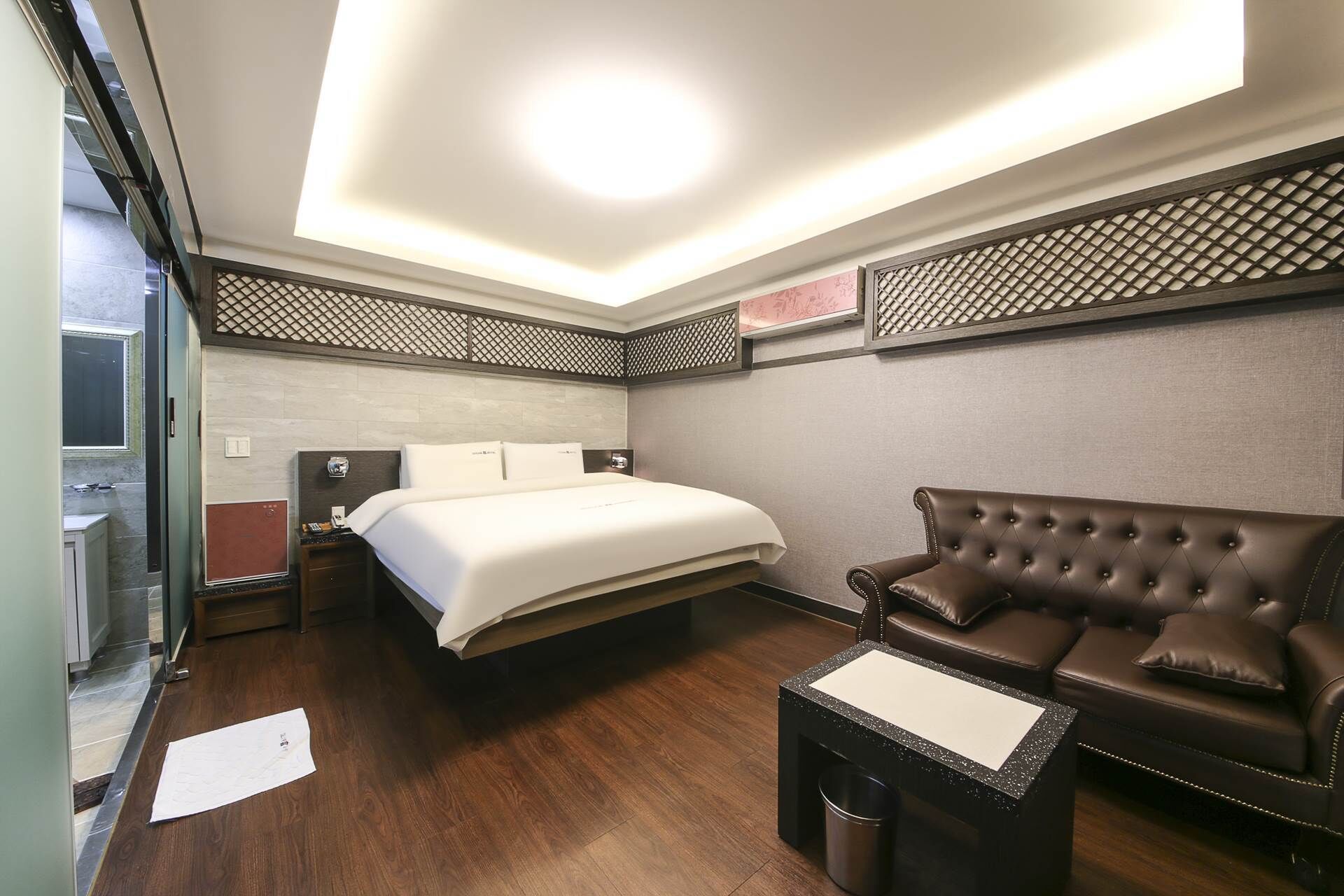Habitación de hotel con cama, sofá de cuero marrón, una mesita y un cesto de basura.