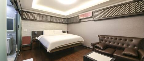 A hotel room with a bed, a brown leather sofa, a small table, and a trash bin.