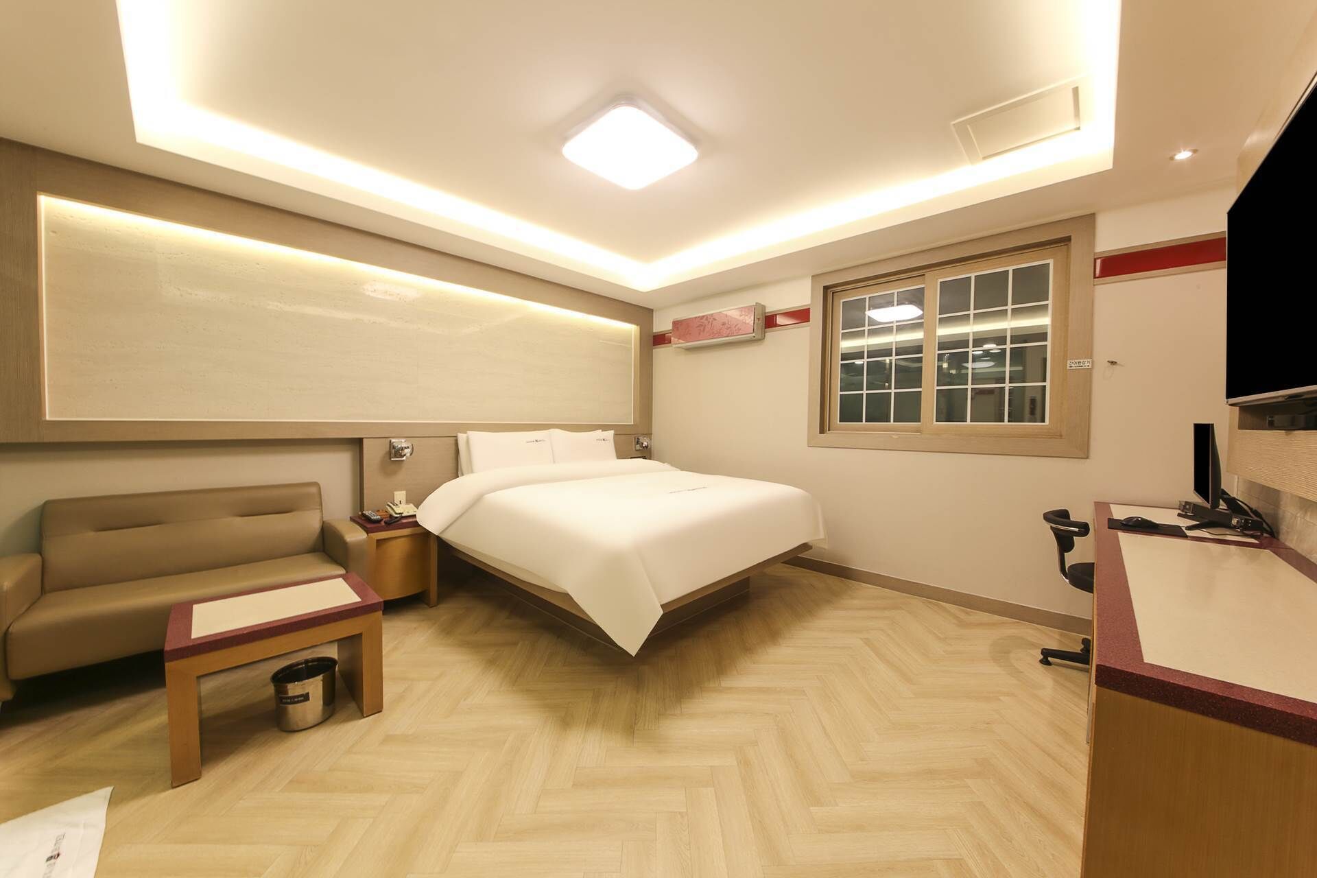 A hotel room with a bed, a desk, a chair, a small table, and a trash bin.
