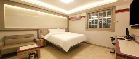 A hotel room with a bed, a desk, a chair, a small table, and a trash bin.
