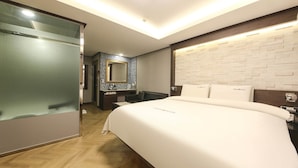 Una habitación de hotel moderna con una cama grande, un baño con espejo y un pequeño rincón de descanso.