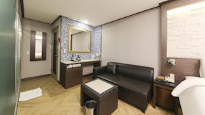 Una habitación moderna con piso de madera, un sofá de cuero negro, una mesita, un espejo y un tocador con artículos de aseo.