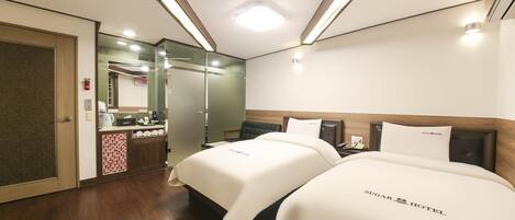 A hotel room with two beds, a bathroom with a mirror, and a wooden floor.