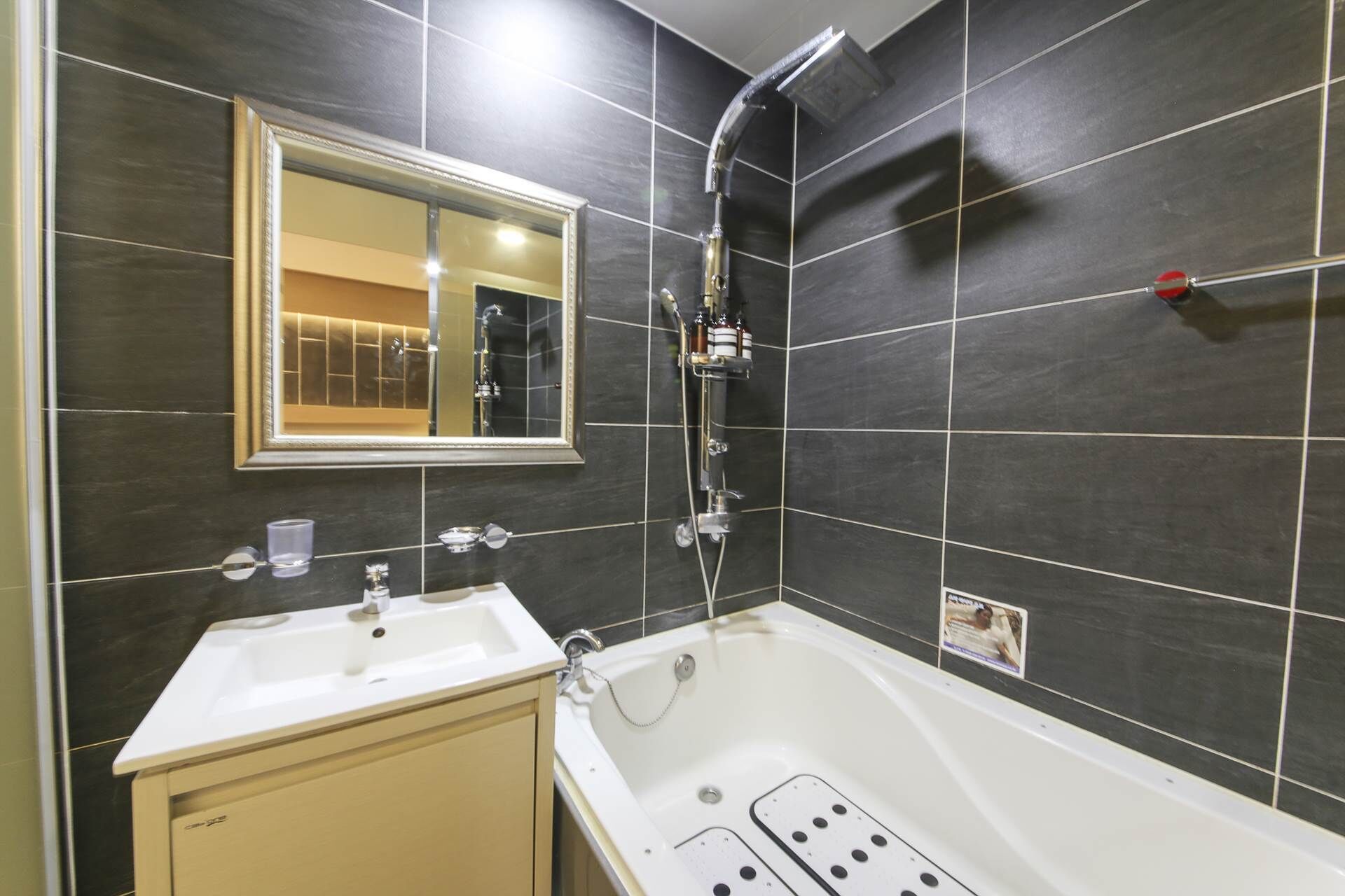 A modern bathroom with a bathtub, a sink, a mirror, and a showerhead.