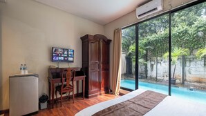 A hotel room with a bed, a desk with a chair, a television, and a view of an outdoor swimming pool. - Arimbi Pejaten Suites (Jakarta)