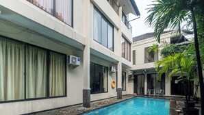 A swimming pool with a stone border, air conditioning units, and a lifebuoy on the wall. - Arimbi Pejaten Suites (Jakarta)