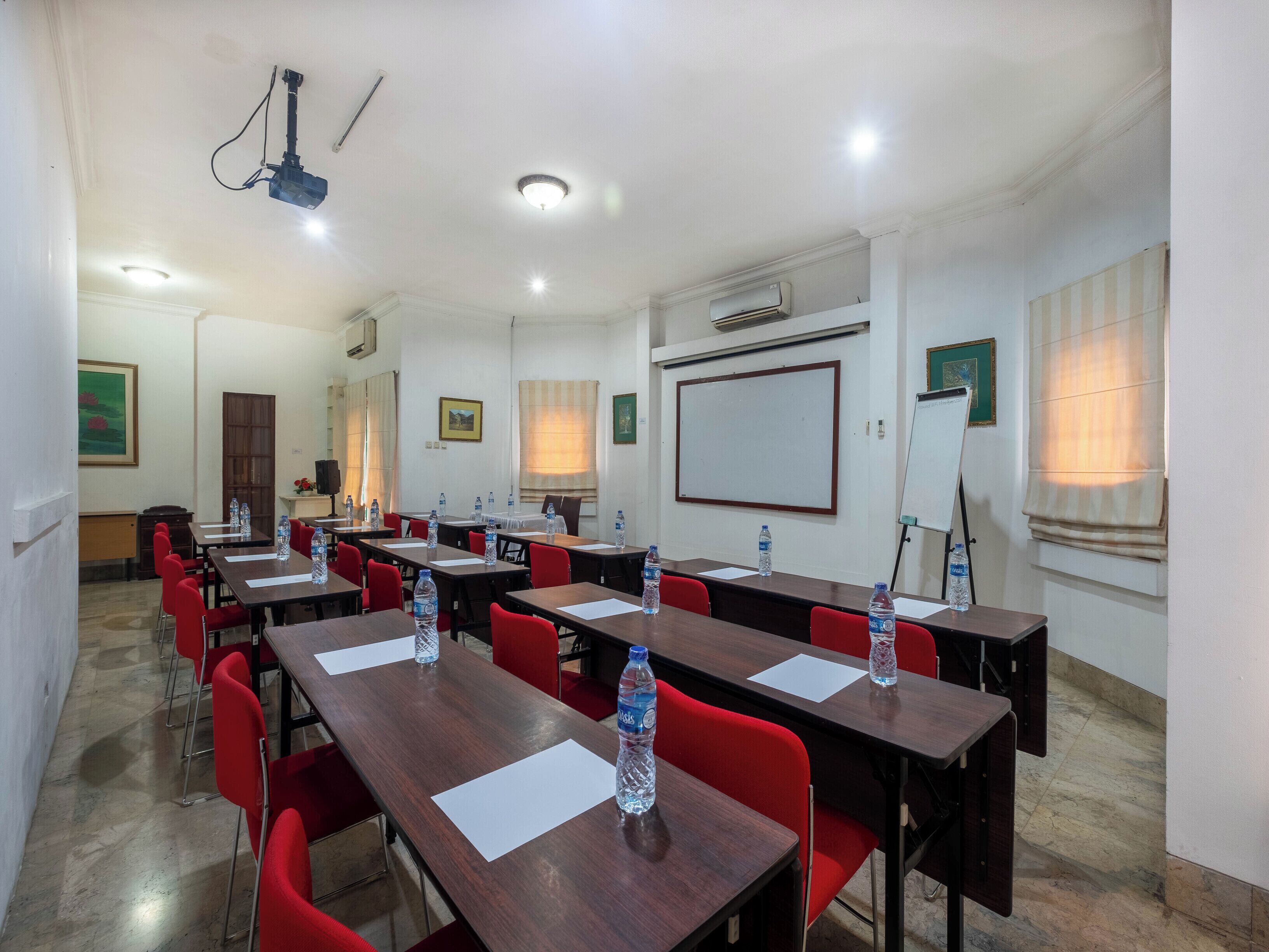 A conference room with multiple tables and red chairs, equipped with water bottles and white papers.