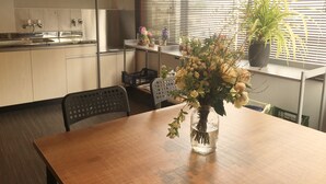 A kitchen with a wooden table, chairs, a vase with flowers, and a window with blinds. - Daikoku House (Osaka)