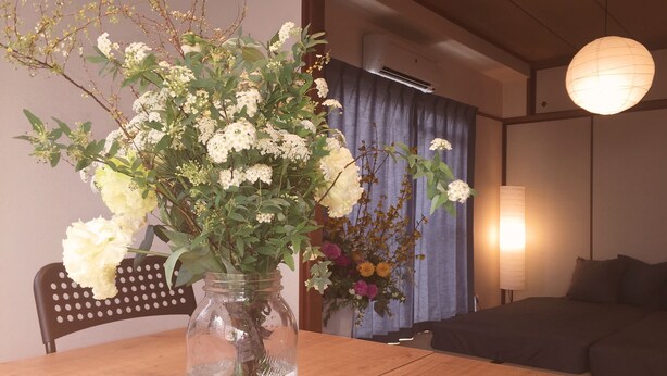 A wooden table with a clear glass vase containing white flowers and green stems. - Daikoku House (Osaka)