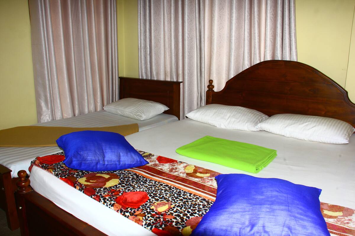 A double bed with a floral bedspread, two blue pillows, and a green folded blanket.