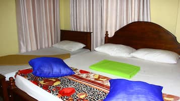Una cama doble con colcha estampada, dos almohadas azules y una manta verde doblada.