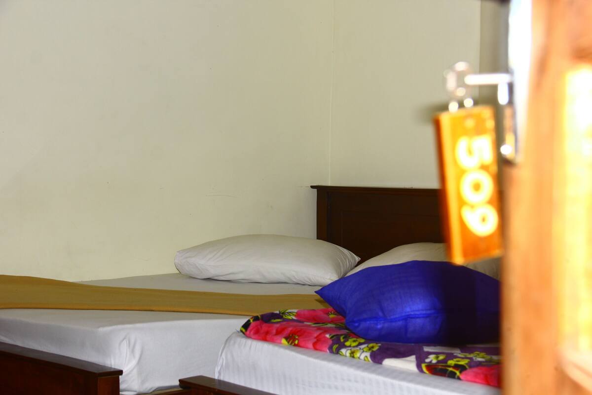 A single bed with white bedding and a floral-patterned blanket, a wooden headboard, and a wall-mounted light fixture.