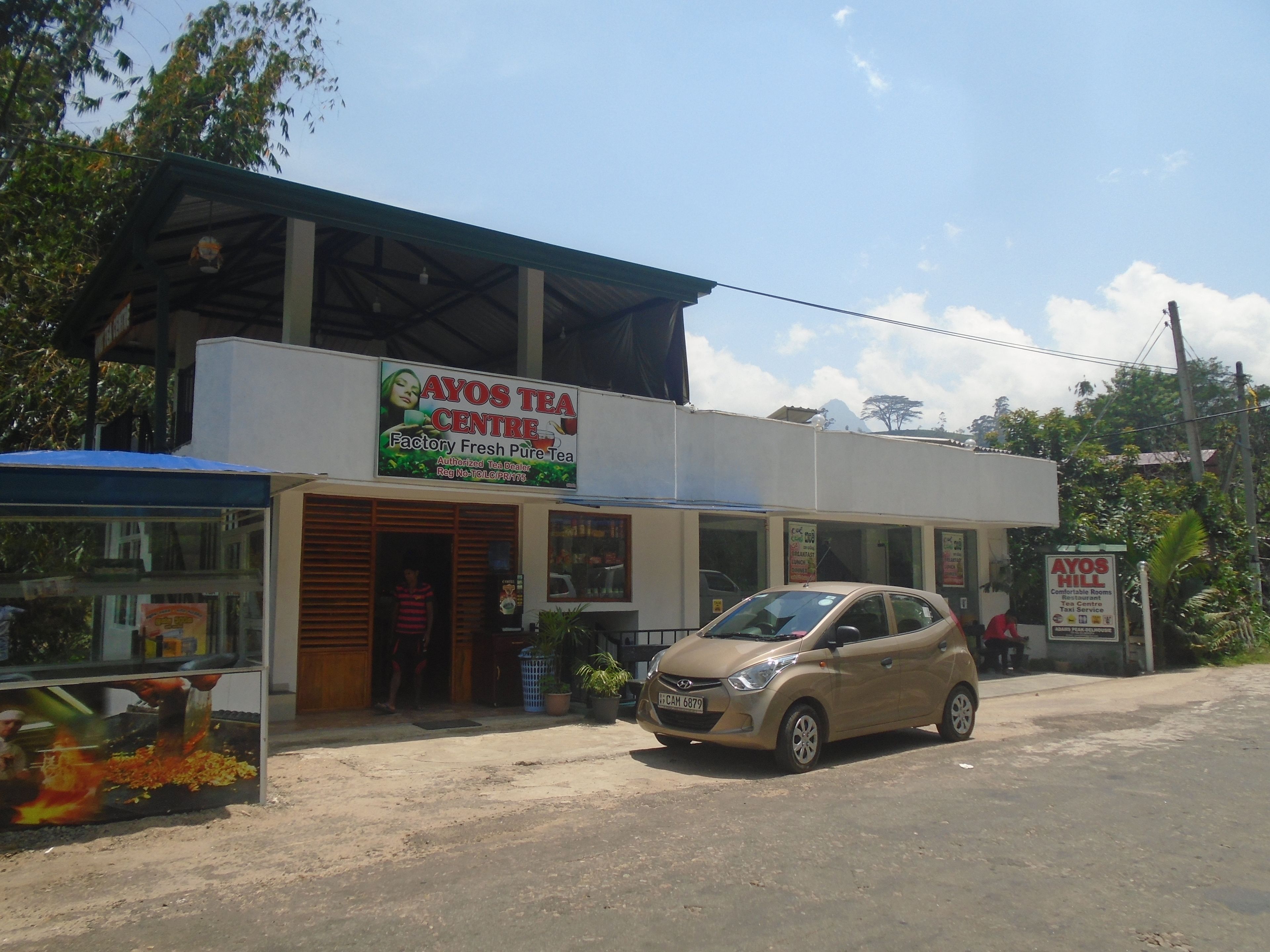 A two-story building with a sign for Ayos Tea Centre, featuring a car parked in front.