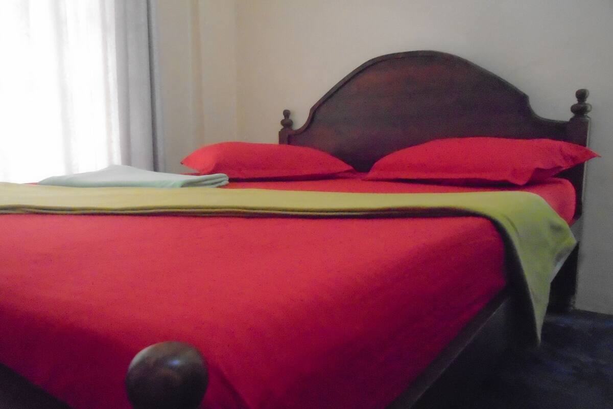 A bed with a wooden headboard, red bedding, and a yellow throw blanket.