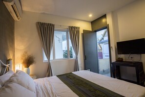 Una camera d'albergo con un letto, un condizionatore d'aria, una TV e una finestra con tende.