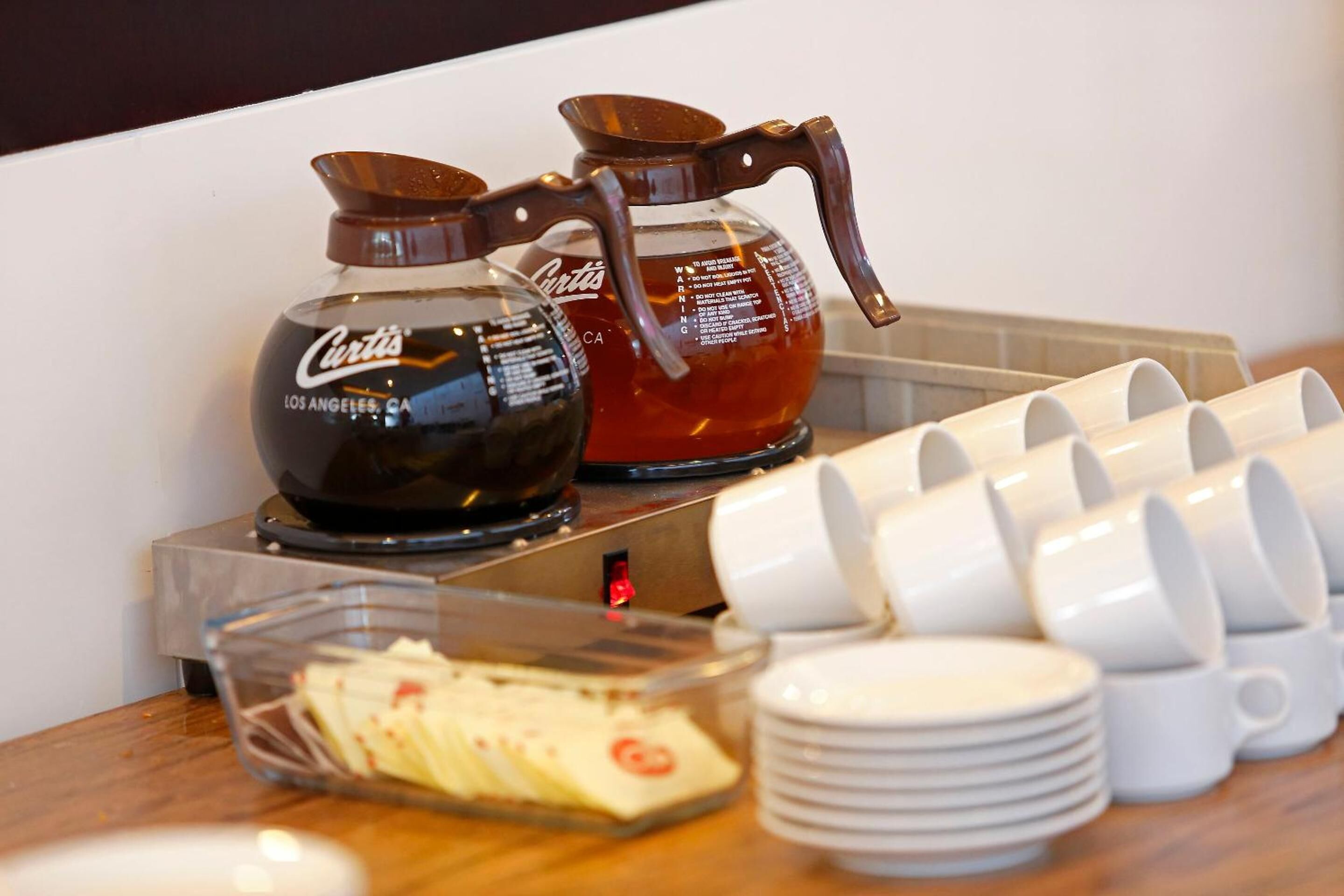 A coffee station with two coffee makers, a tray of pastries, and stacked white cups.