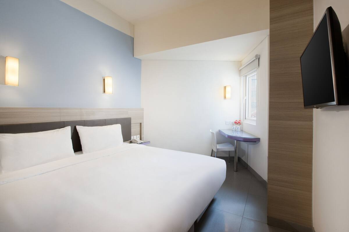 A hotel room with a large bed, bedside tables, a desk, and a flat-screen TV mounted on the wall.