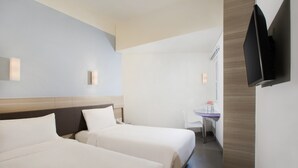 Habitación de hotel con dos camas, un escritorio, una silla y un televisor de pantalla plana montado en la pared.