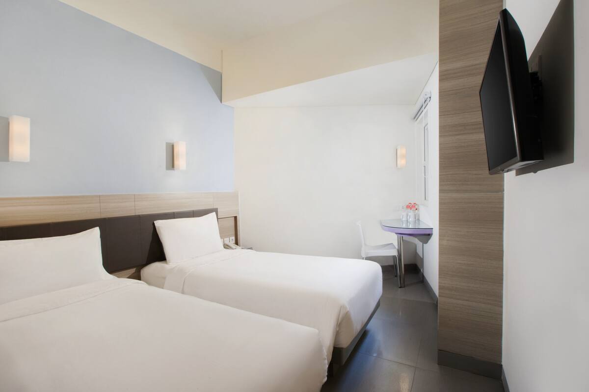 A hotel room with two beds, a desk, a chair, and a flat-screen TV mounted on the wall.