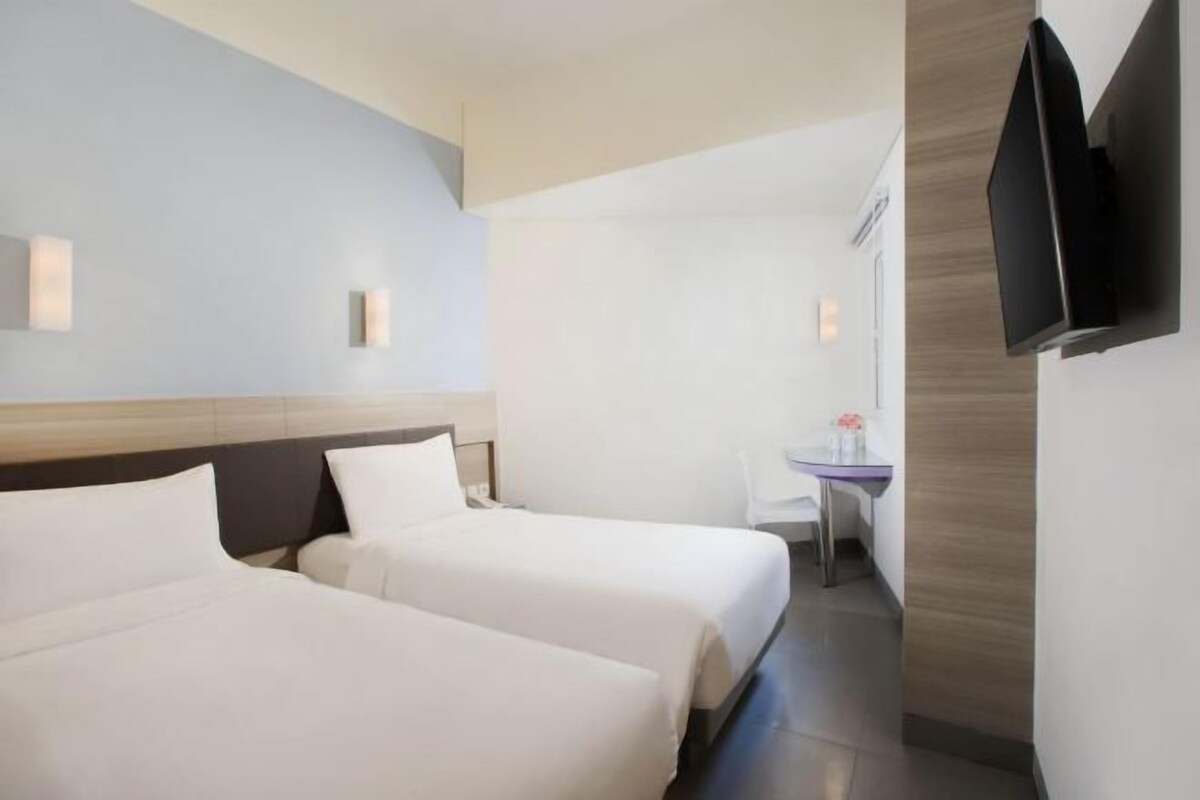 A hotel room with two beds, a small desk, a chair, and a flat-screen TV mounted on the wall.