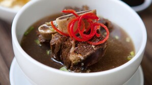 Un tazón de sopa con carne y rodajas de chile rojo sobre un plato blanco.