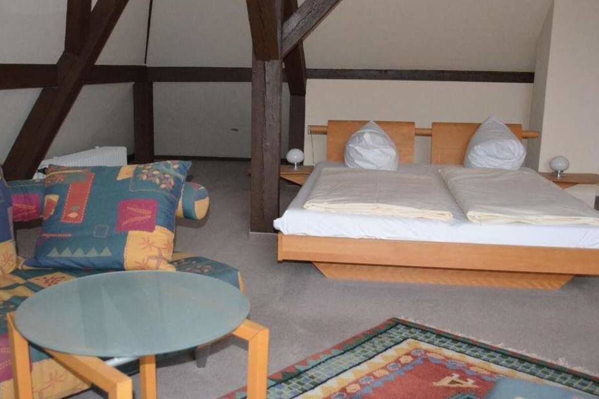 Una habitación con cama, sofá, una mesita redonda y un tapete estampado.