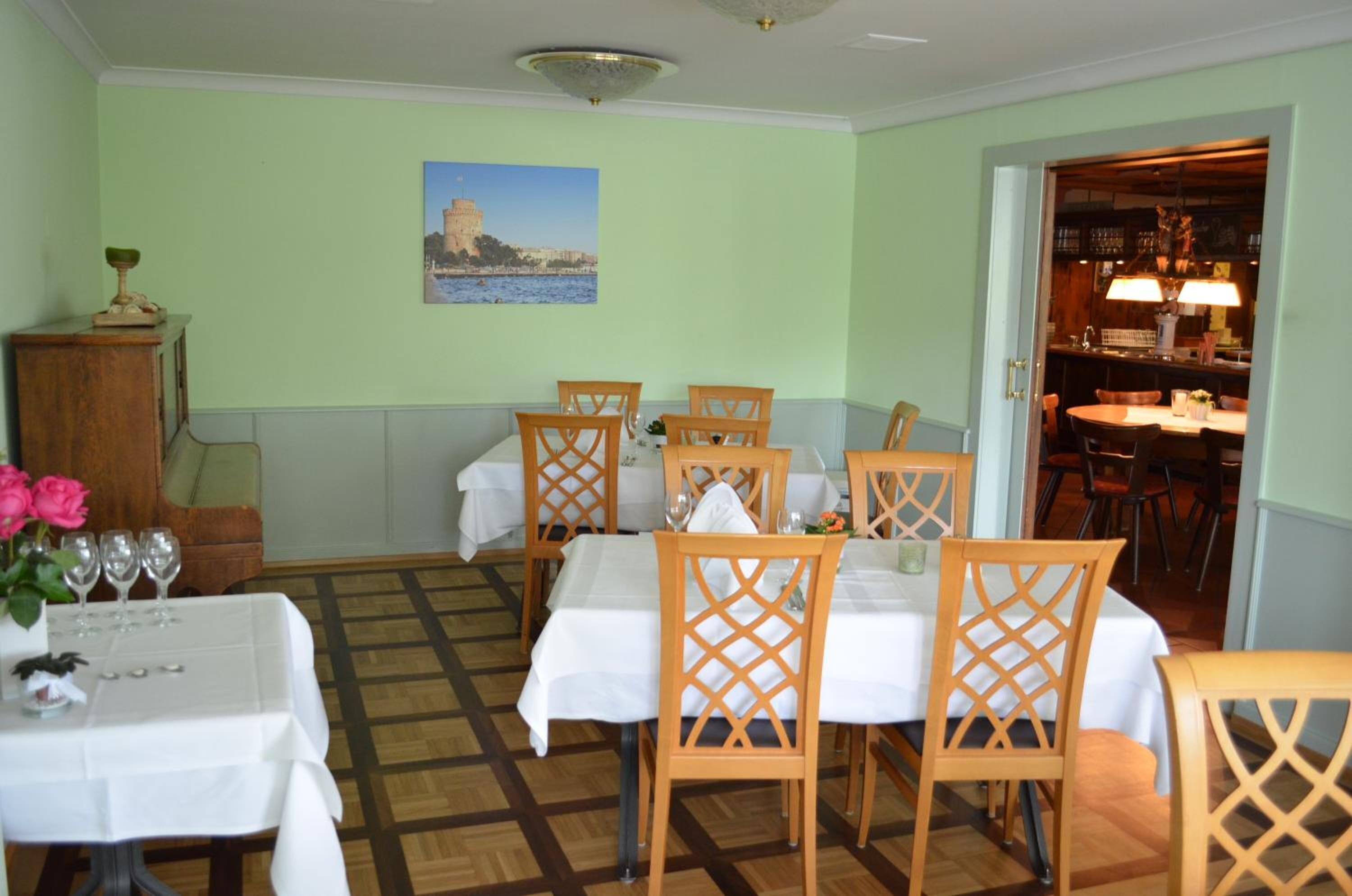 Un espace repas avec des chaises et des tables en bois, une vue sur la mer par une fenêtre et un tableau représentant un paysage côtier.