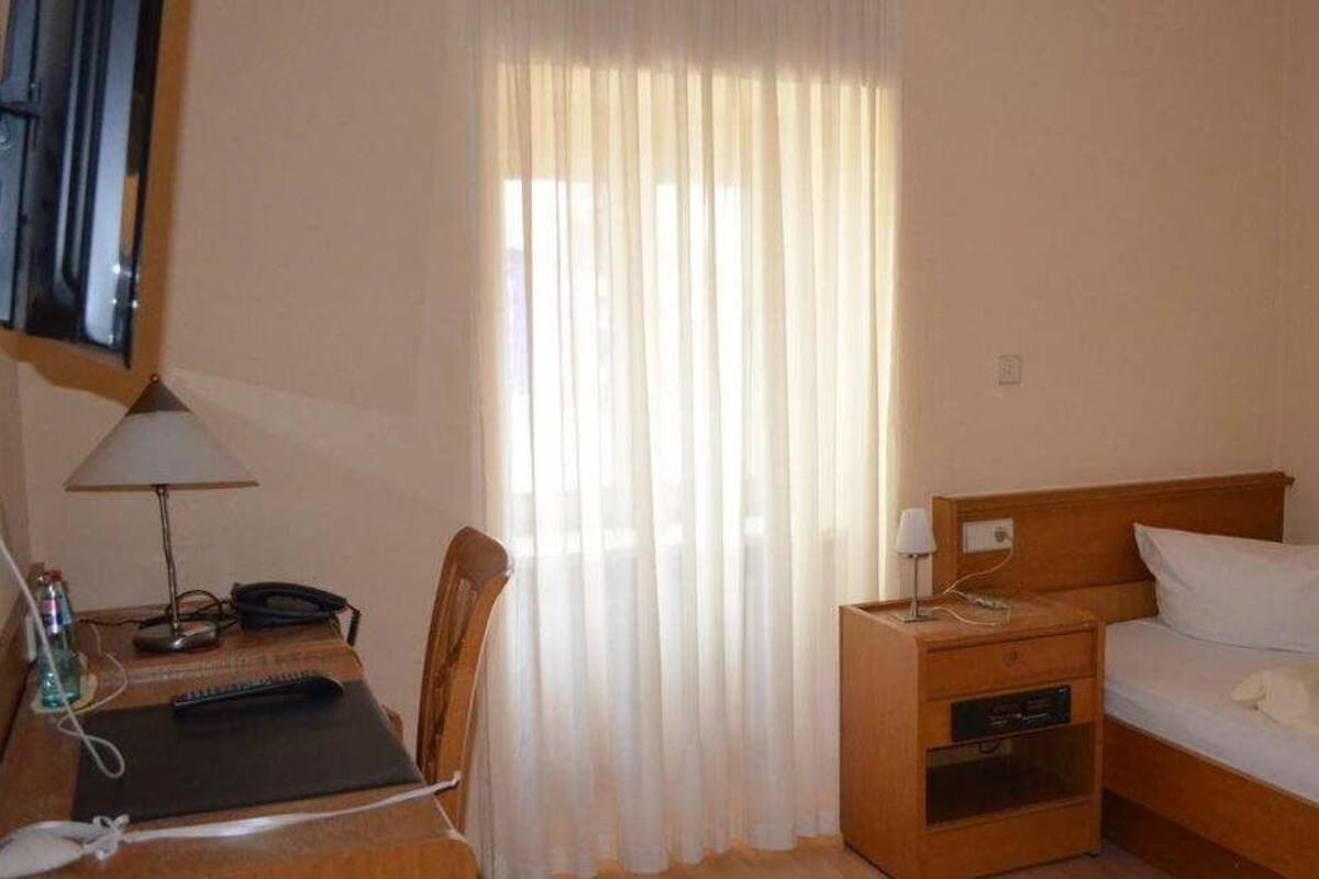 Una habitación de hotel con un escritorio de madera, una silla, una cama con almohada blanca, una mesita de noche y un televisor montado en la pared.