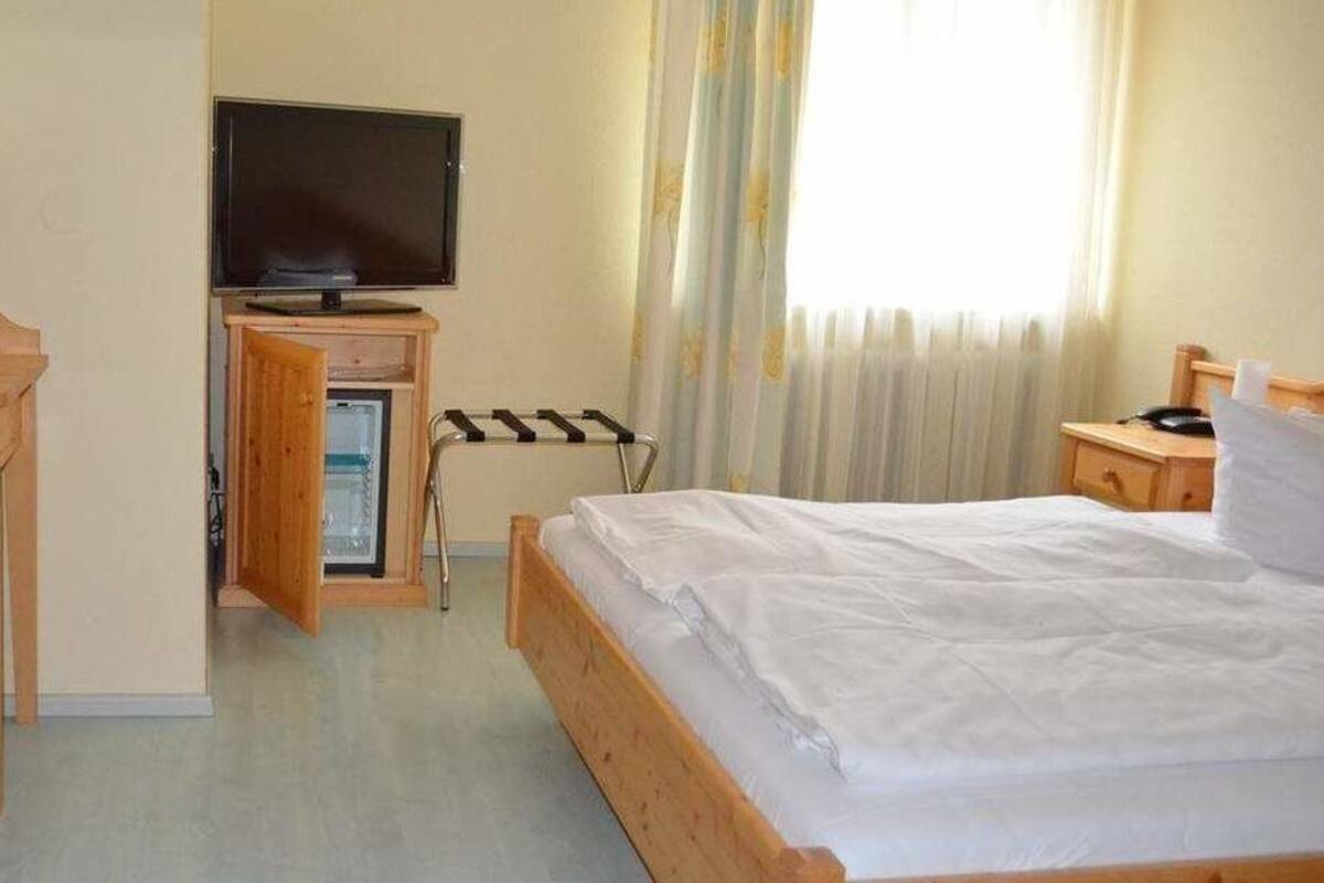 Habitación de hotel con cama, escritorio con silla, televisor y ventana con cortinas.