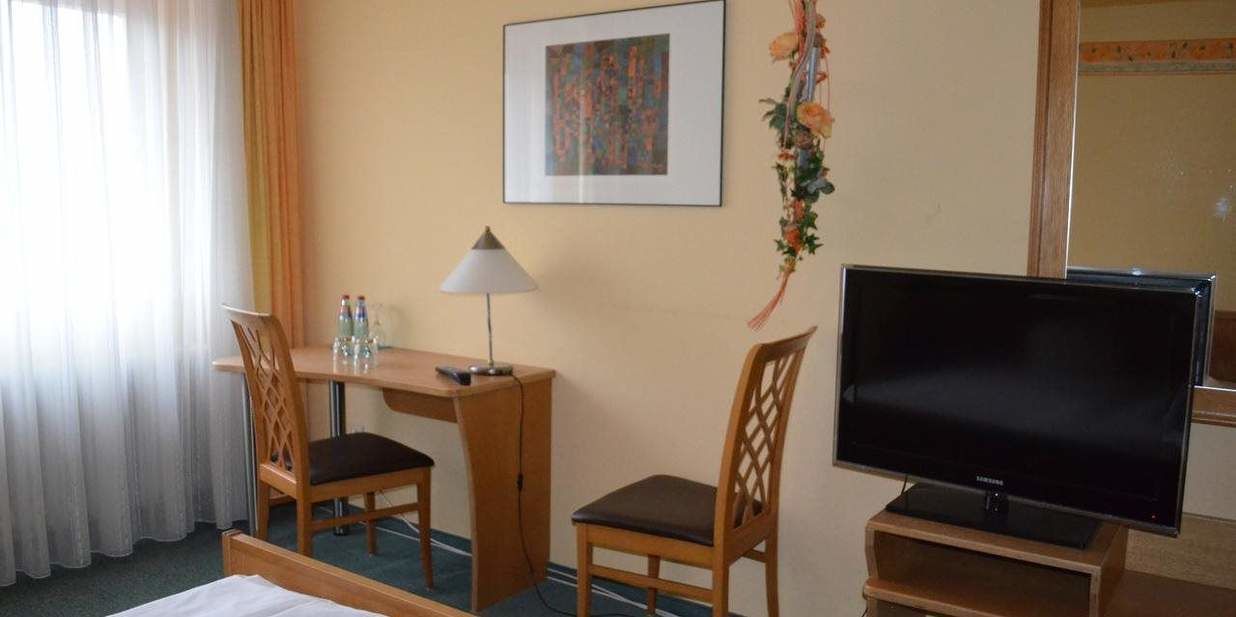 Une chambre d’hôtel comprenant un lit, un bureau avec deux chaises, une télévision et un tableau encadré au mur.