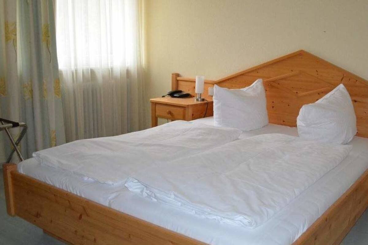 Una cama de madera con ropa de cama blanca, dos mesitas de noche y una lámpara en cada una.