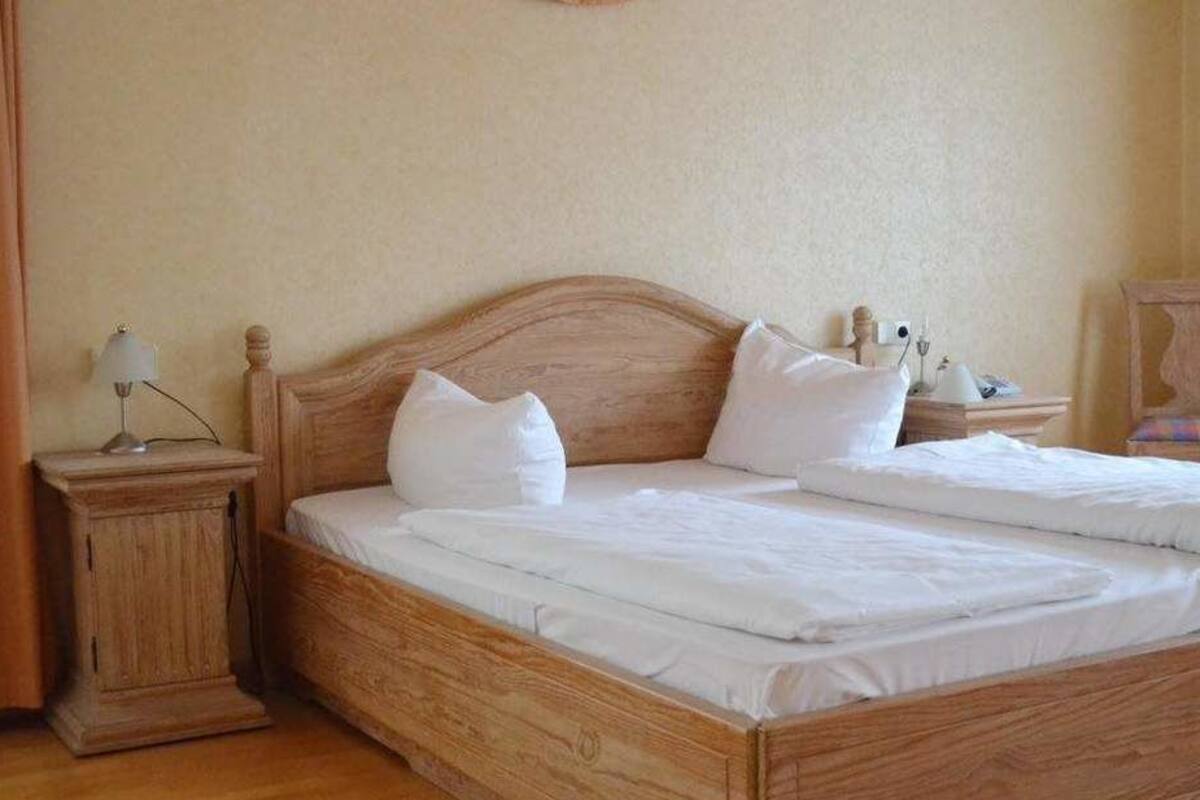 Cama doble con cabecera y piecera de madera, dos mesitas de noche con lámparas y una silla con cojín.