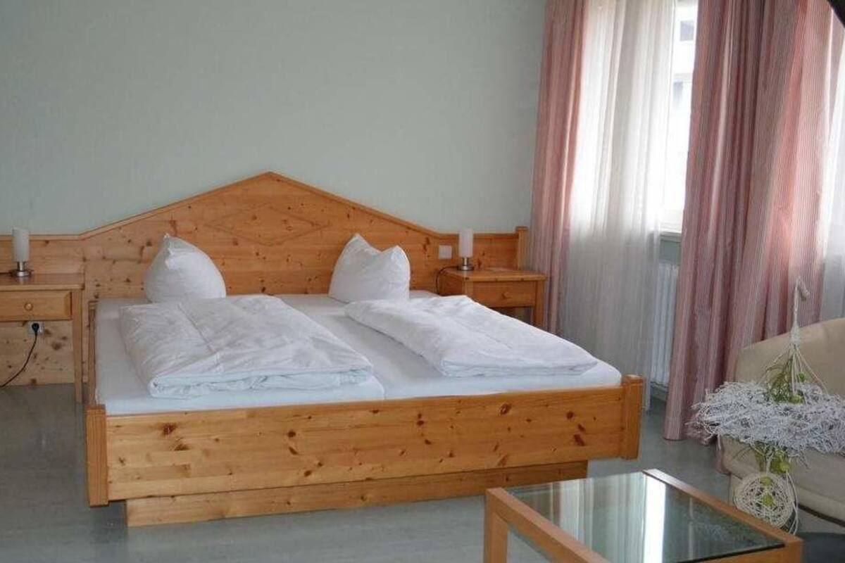 Una cama de madera con sábanas blancas, una mesita de noche, una silla y una mesa de vidrio.